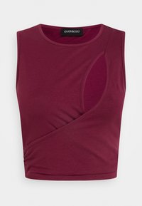 Top cropped sem mangas em bordeaux com um recorte lateral e detalhes drapeados, feito de um tecido macio e elástico. Textura lisa com decote arredondado.