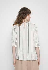 Blusa às riscas em branco com detalhes em tons pastel. Apresenta mangas bufantes, punhos franzidos e um detalhe de decote em gota nas costas. Tecido leve.