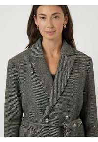 Gestreepte blazer van wolmix met een double-breasted voorkant, brede revers, twee knopen en een ceintuur om te strikken. Kleuren zijn zwart en wit.