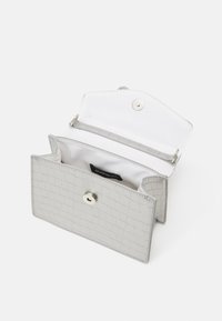 Portefeuille en cuir de crocodile gris clair avec fermeture à bouton pression, présentant un intérieur blanc et une étiquette, ouvert pour révéler deux compartiments.