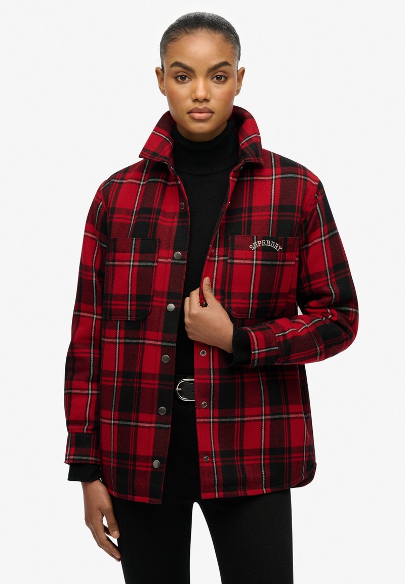Red and black plaid flannel jacket with two chest pockets, snap buttons, and a high collar. Fabric appears soft with a cozy texture.