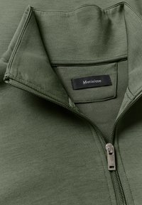 Felpa verde con zip, caratterizzata da un colletto alto, una texture liscia e una zip argentata. L'etichetta del marchio "Matinique" è visibile all'interno.