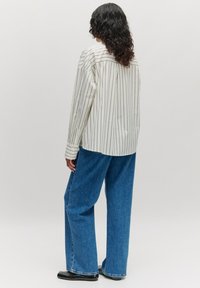 Weiß gestreiftes Hemd mit lockerem Schnitt, kombiniert mit weit geschnittenen blauen Jeans. Verfügt über einen Kragen und lange Ärmel.