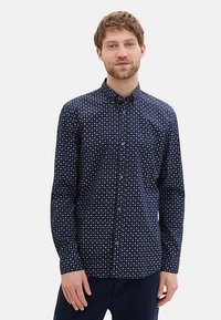 Chemise bleu marine à manches longues avec un petit motif géométrique blanc et des boutons, dotée d'un col classique et d'une coupe ajustée.