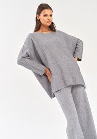 Szary wełniany sweter i dopasowane spodnie, o luźnym kroju, szerokich rękawach i gładkiej teksturze. Prosty i minimalistyczny design, bez wzorów.