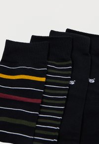 Τέσσερις ζευγάρια κάλτσες σε σκούρους τόνους, με διάφορα μοτίβα: ένα με οριζόντιες ρίγες σε κίτρινο, μπορντό και λευκό, και άλλο με στενές πράσινες και λευκές ρίγες.