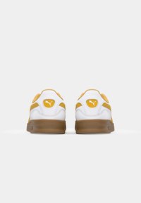 Hvite sneakers med gule detaljer, med en glatt læroverdel, polstret krage og såle av gummigummi. Puma-logo på hælen.