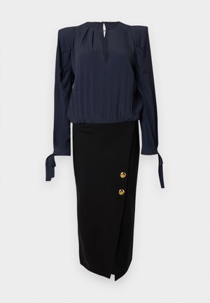 Tumesinine pluus patsikleitud varrukatega ja avaga kaelusel, kombineeritud musta pliiatsseelikuga, millel on kuldsete nuppude detailid küljel.