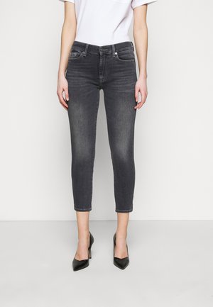 Woman wearing faded black cropped skinny jeans paired with black pointed-toe high heels and a white short-sleeve top.