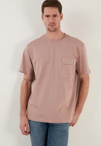 Ljust rosa bomull t-shirt med korta ärmar, rund halsringning och framficka. Har en rak passform och subtila sömnadsdetaljer.