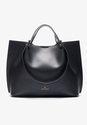 Sac cabas en cuir noir avec deux anses et logo doré "ANNA FIELD" centré près du bas.