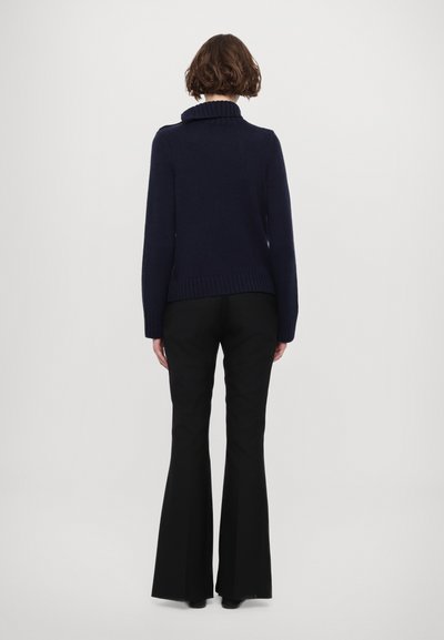 Pull en maille navy avec un col haut en côtes et des manches longues, associé à un pantalon noir à pattes d'éléphant. Le pull présente une silhouette ajustée.
