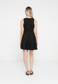 Robe noire sans manches avec une jupe évasée, fabriquée dans un tissu lisse. Elle présente un buste simple et ajusté et tombe au-dessus du genou.