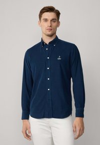 Marineblauw overhemd met lange mouwen, van zachte stof, met een klassieke kraag, witte knopen en een geborduurd logo op de borst.