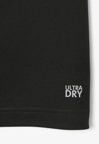 Maglietta sportiva nera in tessuto a rete texturizzato. Presenta il logo "ULTRA DRY" in bianco nell'angolo in basso a destra.