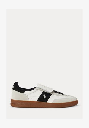 Sneaker blanc basse avec bande noire, semelle marron et logo brodé sur le côté, avec talon bordé de noir et bride velcro sur les lacets.