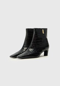 Bottines noires à bout pointu, en cuir verni embossé crocodile, avec un petit talon carré et un accent doré.