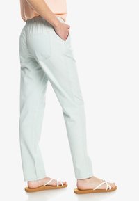 Pantalones verde menta claros con cintura elástica, diseño de pierna recta y dos bolsillos traseros, combinados con sandalias planas.