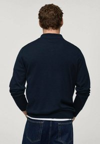 Maglione in maglia di colore blu navy con colletto rotondo e maniche lunghe, caratterizzato da una superficie liscia e dettagli minimi sulle spalle e sui polsini.