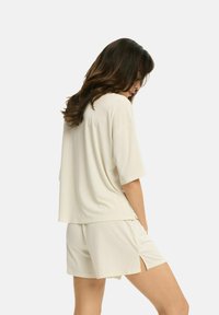 Jasne, kremowe zestaw loungewear składający się z luźnej bluzki z krótkim rękawem oraz pasujących szortów z bocznymi rozcięciami dla łatwości ruchów.