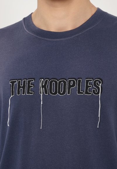 Námořnické modré bavlněné tričko s kontrastním černým vyšitým logem "THE KOOPLE" a volnými nitěmi. Standardní střih s kulatým výstřihem.