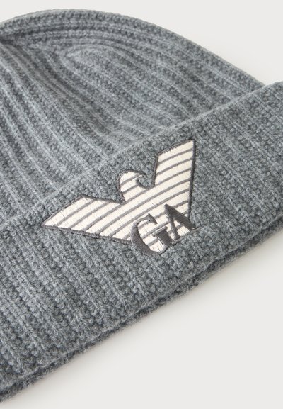 Bonnet en tricot côtelé gris avec bord replié, arborant un écusson logo aigle rayé blanc et gris avec les lettres "GA" à l'avant.