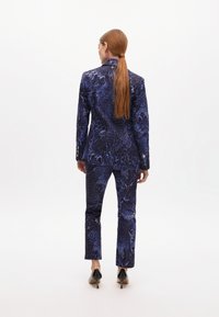 Blaues gemustertes Anzugset mit tailliertem Blazer und schmalen Hosen. Auffällige Textur mit einem kühnen Tierdruck. Tragen mit schwarzen High Heels.