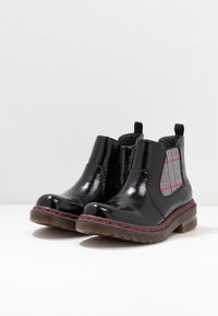 Svarta blanka läderankelboots med röda sömmar, rutiga elastiska sidopaneler och bruna gummisulor på en vit yta.