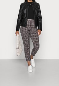 Black leather jacket, black knit top, plaid trousers in brown and white, white sneakers, and a white woven bag.