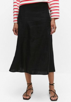 Kvinde iført en sort midinederdel, rød- og hvidstribet langærmet top og sorte flade sandaler med stropper, stående foran en hvid baggrund.