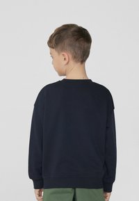 Námořnická modrá mikina s kulatým výstřihem, volným střihem a dlouhými rukávy, s žebrovanými manžetami a lemem. Pohled ze zad.