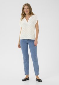 Hvid strikbluse med diamantmønster, kortærmede og V-hals. Kombinationen med lyseblå jeans og sorte ballerinaer. Enkel, åndbar design.