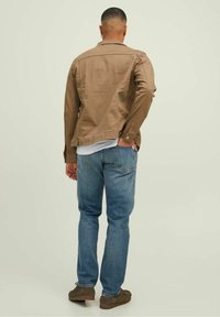 Brun bomullskavaj med knapppynt, kombinerad med blå denimjeans. Avslappnade skor fulländar looken. Vy från baksidan.