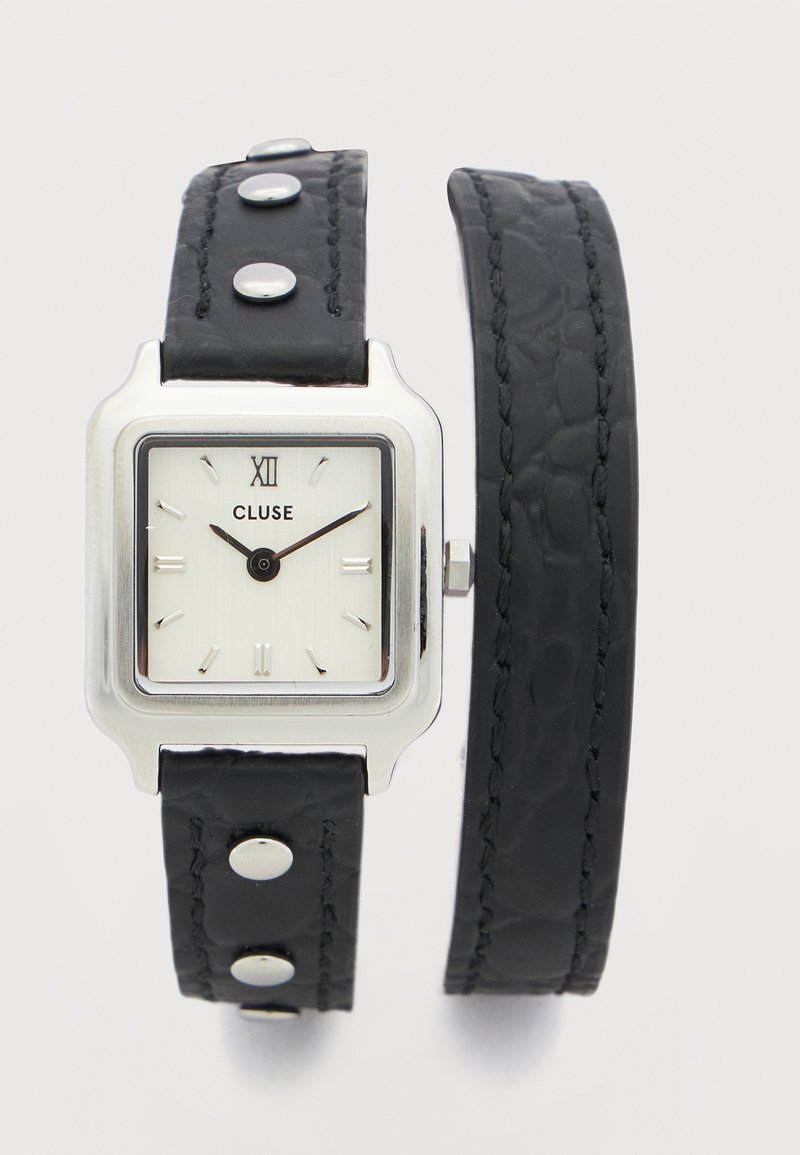 Τετράγωνο ασημί ρολόι με λευκό καντράν, μαύρα δείκτες ώρας και λεπτών, μαύρο δερμάτινο λουράκι διπλής περιέλιξης με ασημένιες καρφίτσες.