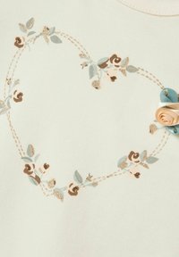 Lys grøn stof med et hjerteformet blomstermotiv, der har brune og blå blade, gyldne accenter og en båndblomstdetalje.