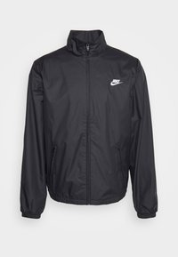 Svart vindjacka med hög krage, blixtlås framtill och Nike-logotyp. Har elastiska muddar och sidofickor för praktisk användning.