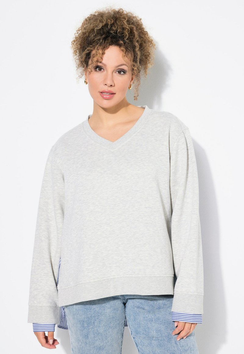 Sudadera gris claro con escote en V, mangas largas y puños a rayas azul y blanca. Cuenta con un corte relajado y una textura suave.