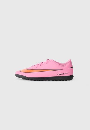 Pinker Nike Mercurial Fußballschuh mit schwarzer Sohle und orangefarbenem Swoosh-Logo, seitlich auf grauem Hintergrund dargestellt.