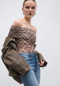 Καρό τοπ σε καφέ και μπεζ αποχρώσεις με έναν ώμο έξω, συνδυασμένο με μια χαλαρή καφέ δερμάτινη μπουφάν και τζιν παντελόνι σε ανοιχτό μπλε. Απαλές υφές με πολυεπίπεδες λεπτομέρειες.