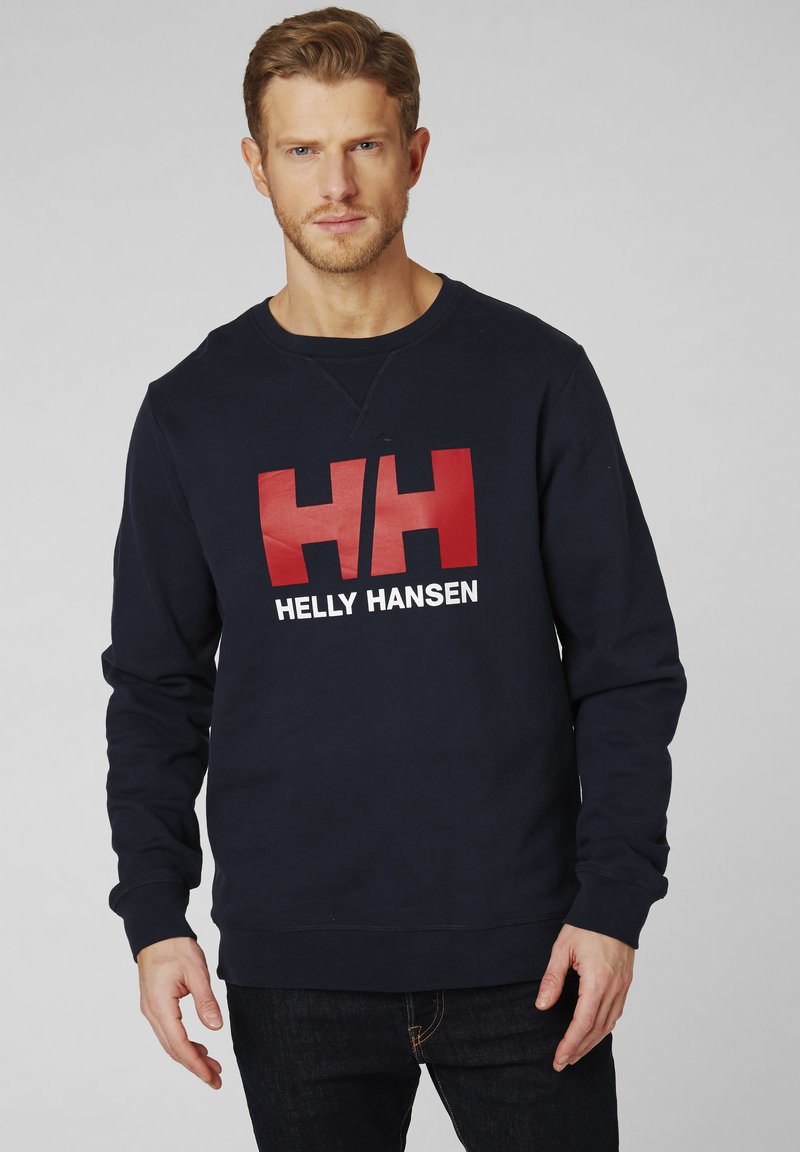 Námořnická modrá mikina s kulatým výstřihem a dlouhými rukávy, s výraznými červenými písmeny "HH" a "HELLY HANSEN" v bílé barvě. Klasický střih.