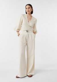 Kremowa bluzka z baskinką i krótkimi, bufkami, zestawiona z spodniami o wysokim stanie i szerokimi nogawkami, oraz czarnym paskiem. Płaskie sandały uzupełniają cały look.