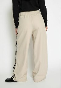 Beige wide-leg pants with an elastic waistband, featuring black side stripes. Smooth texture, completed with black shoes.