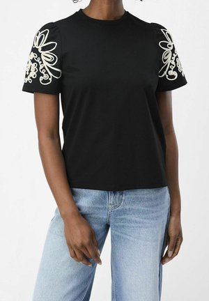 Black cotton t-shirt with puff sleeves, featuring white floral embroidery on the shoulders. Paired with light blue wide-leg jeans.