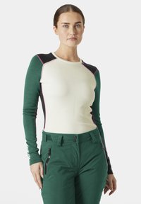 Dlouhý rukáv s bílým tělem, zelenými rukávy a černými rameny, zdobený růžovým šitím. V kombinaci s lesně zelenými kalhotami a kapsami na zip.