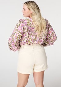 Bloem blouse met roze en groene patronen, knoopsluiting en pofmouwen, gecombineerd met crèmekleurige opgerolde shorts met achterzakken.