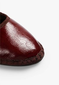 Zapato de cuero burdeos con un acabado brillante, puntera afilada, borde texturizado y detalles cosidos alrededor del perímetro.