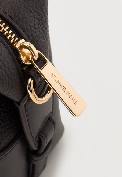 Gros plan d'un sac en cuir noir avec une fermeture éclair dorée et un tire-zip en or poli gravé Michael Kors.