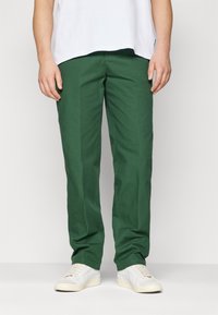 Green cotton trousers with a straight fit, featuring side pockets and a smooth texture, paired with white sneakers at the bottom.