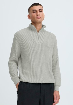 Hellgrauer Pullover mit hohem Kragen, ausgestattet mit einem halben Reißverschluss und geripptem Muster. Lange Ärmel, entspannte Passform.