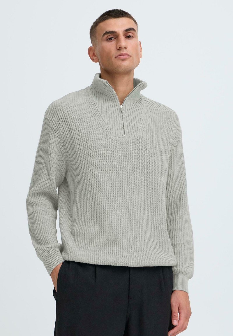 Hellgrauer Pullover mit hohem Kragen, ausgestattet mit einem halben Reißverschluss und geripptem Muster. Lange Ärmel, entspannte Passform.